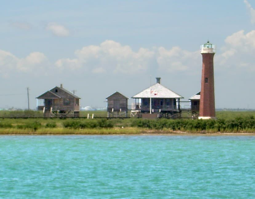 The Lydia Ann Lighthouse near Port Aransas — historic red-brick conical tower standing over the Lydia Ann Channel, with green coastal marsh and clapboard quarters at its base.