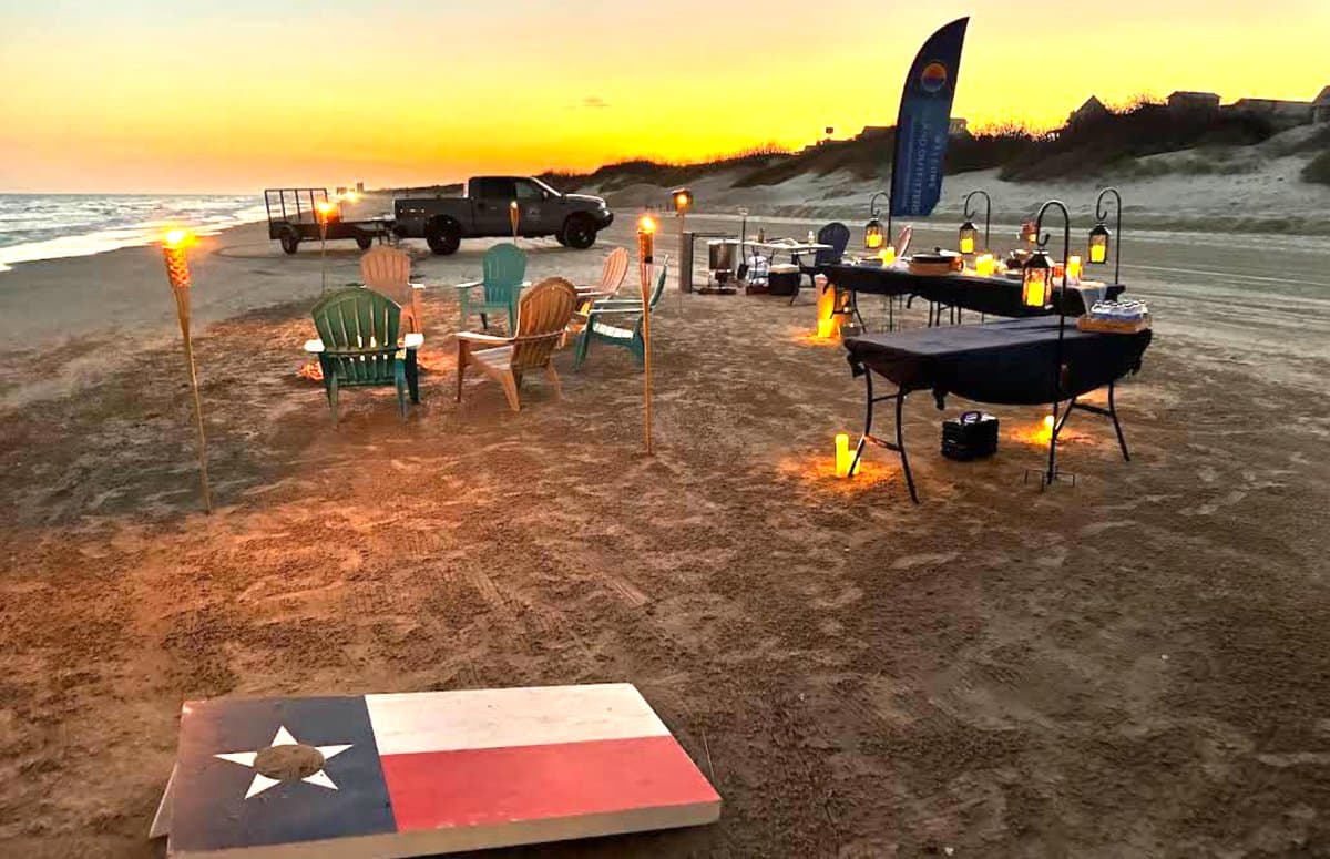 Beachfront shrimp boil at sunset with Island Outfitters in Port Aransas — Adirondack chairs, tiki torches, lanterns and a buffet table on the sand