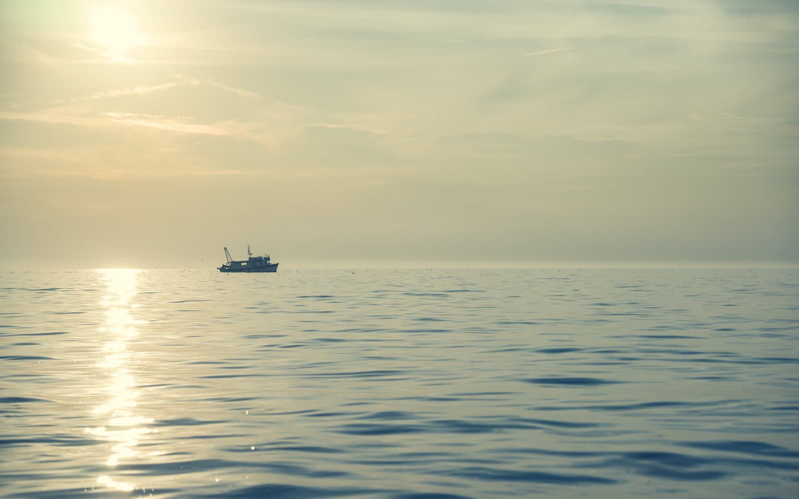 Small fishing boat silhouetted on calm open water in warm sunset light.