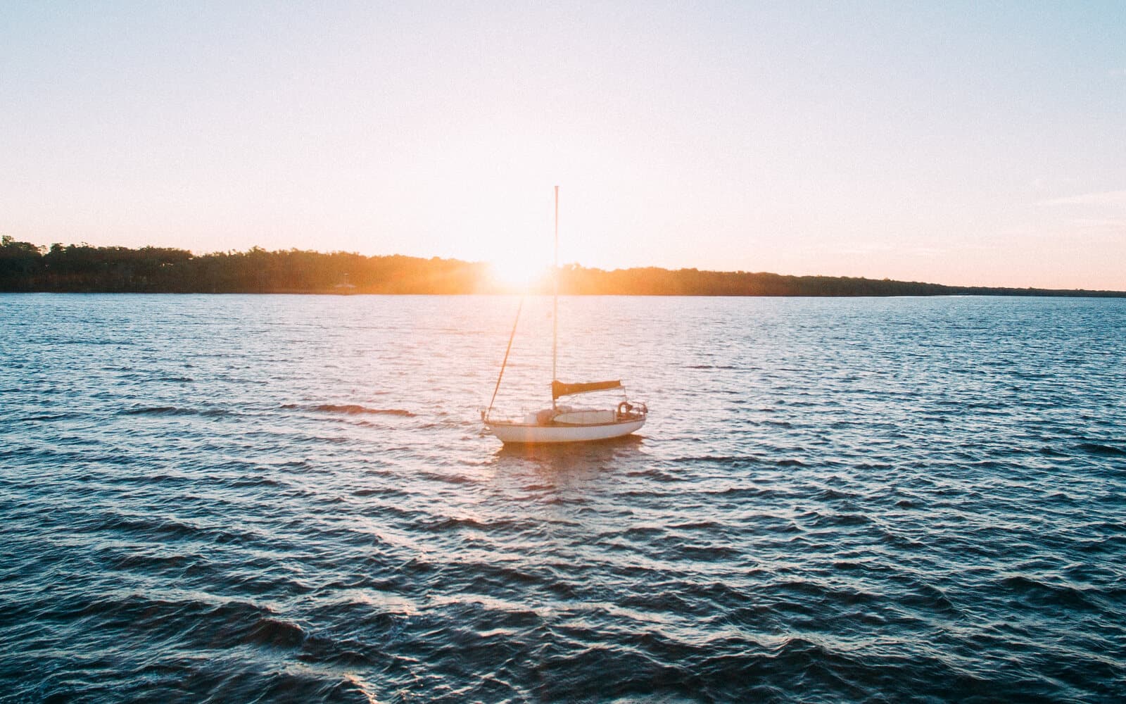 Small sailboat on rippled blue water at sunset, with golden light spreading across the bay.