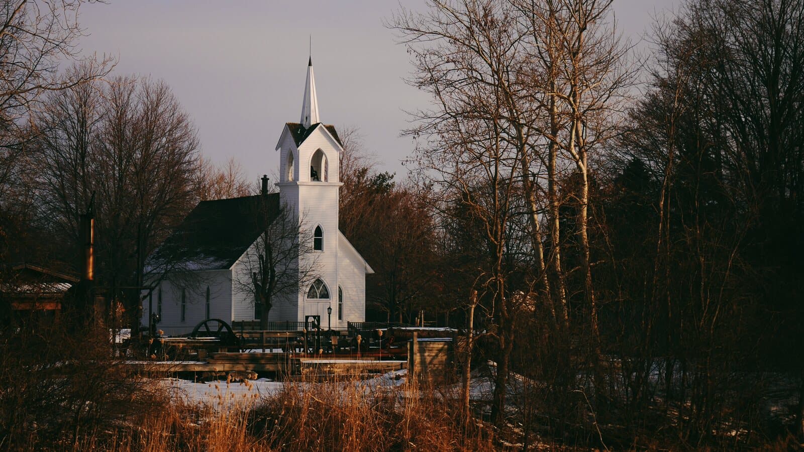 Small white chapel with a steeple and bell tower framed by trees at golden hour - representative licensed image for Chapel On The Dunes pending an exact licensed Port Aransas photo.