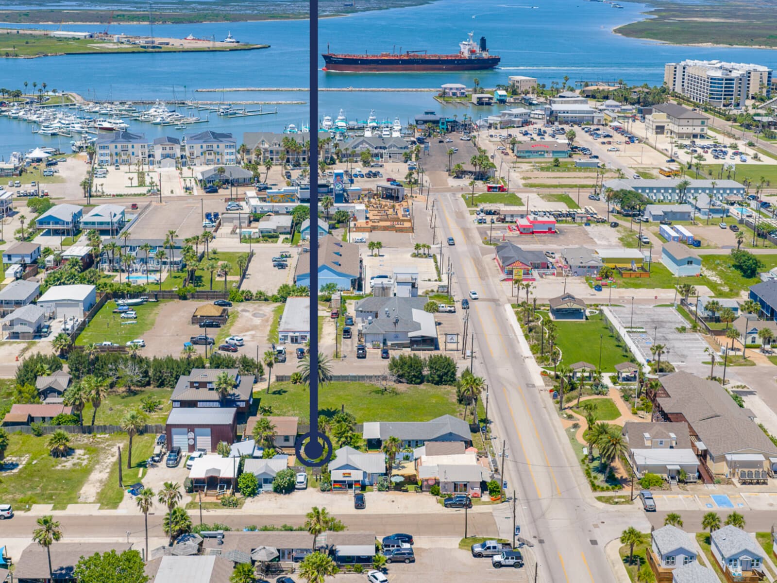 Aerial view of Port Aransas's Old Town — small clapboard houses on a tight grid of streets running down to the marina, the channel and Aransas Pass visible beyond with a tanker passing.