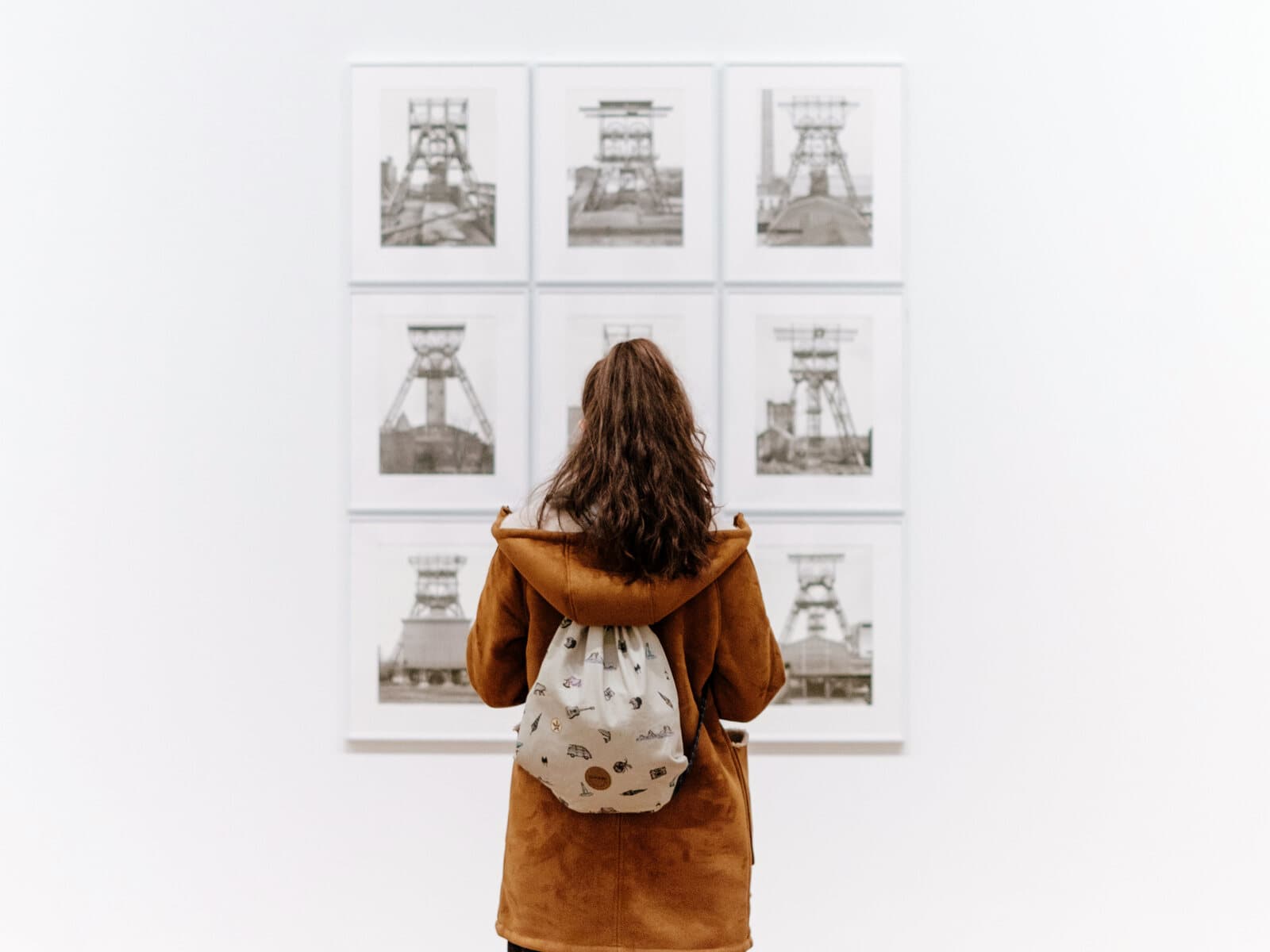 Visitor with a backpack studying framed artwork on a bright white gallery wall - representative of the exhibition rooms at the Port Aransas Art Center.
