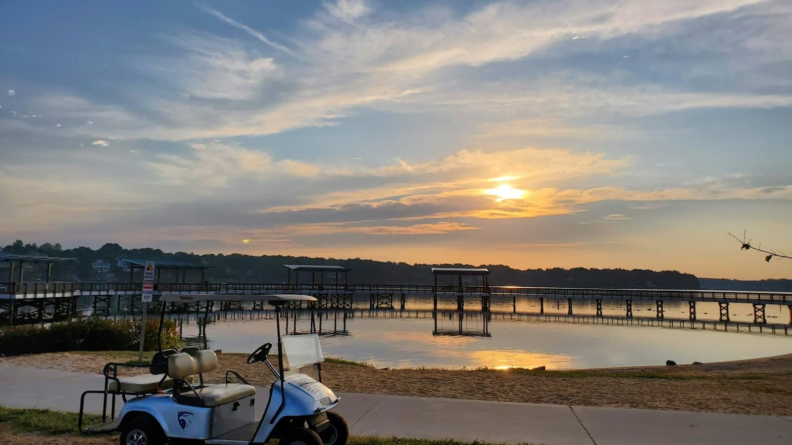 White golf cart parked near a waterfront beach path at sunset, with a dock and calm water behind - representative of beach cart rentals around Port Aransas.
