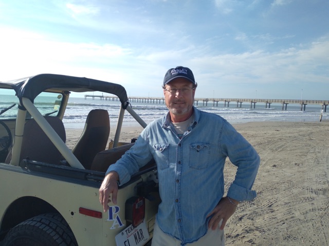 Will Foster, Port Aransas REALTOR® with eXp Realty, on the beach beside his Jeep